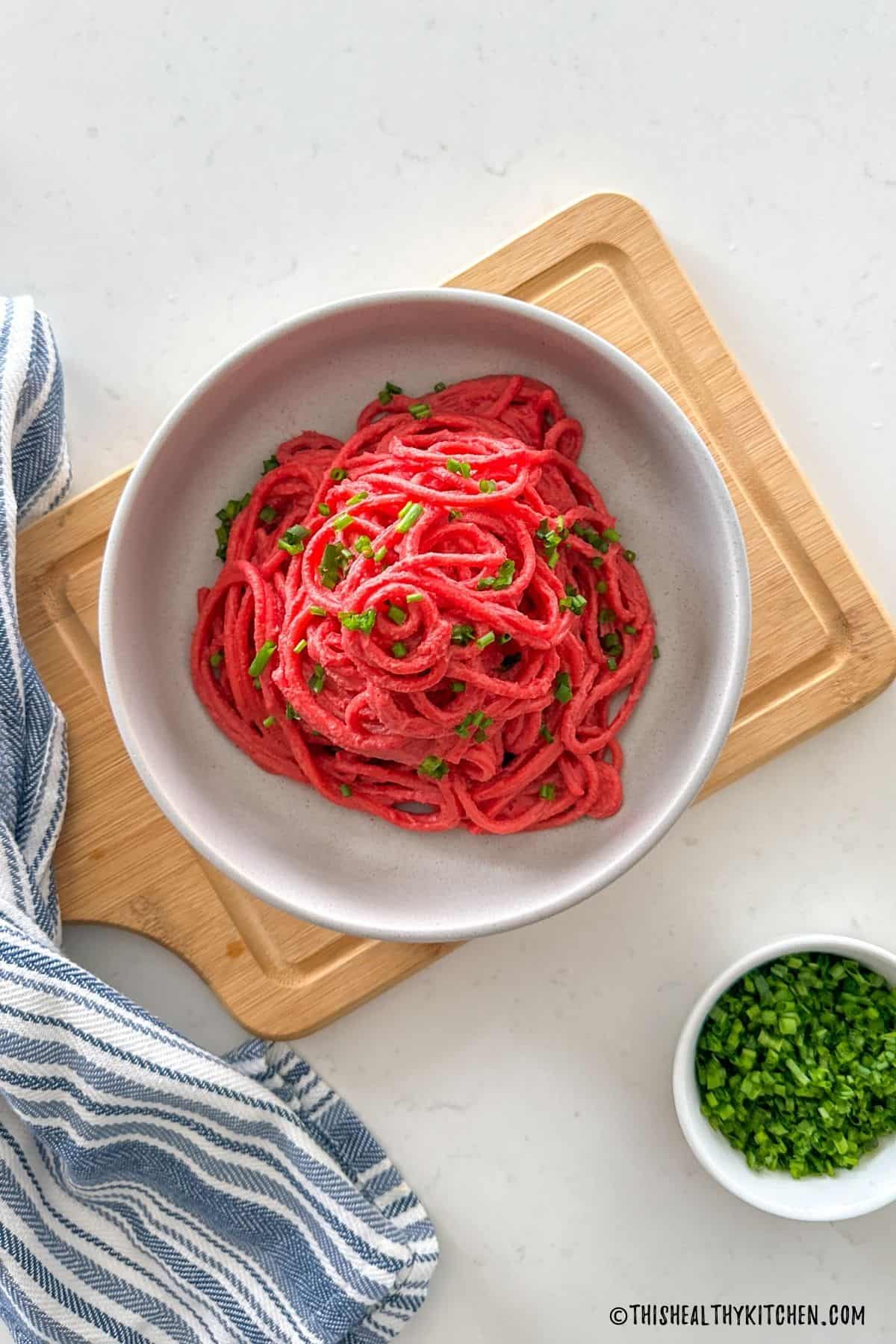 Bowl of spaghetti with red beet sauce and chopped chives on top.