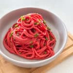 Grey bowl with spaghetti piled high with beet sauce and chives on top.