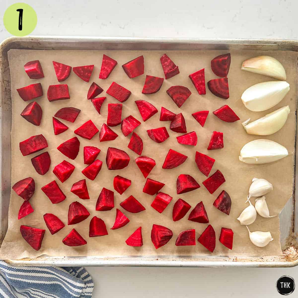 Chopped beets, onion and garlic cloves on baking tray lined with parchment paper.