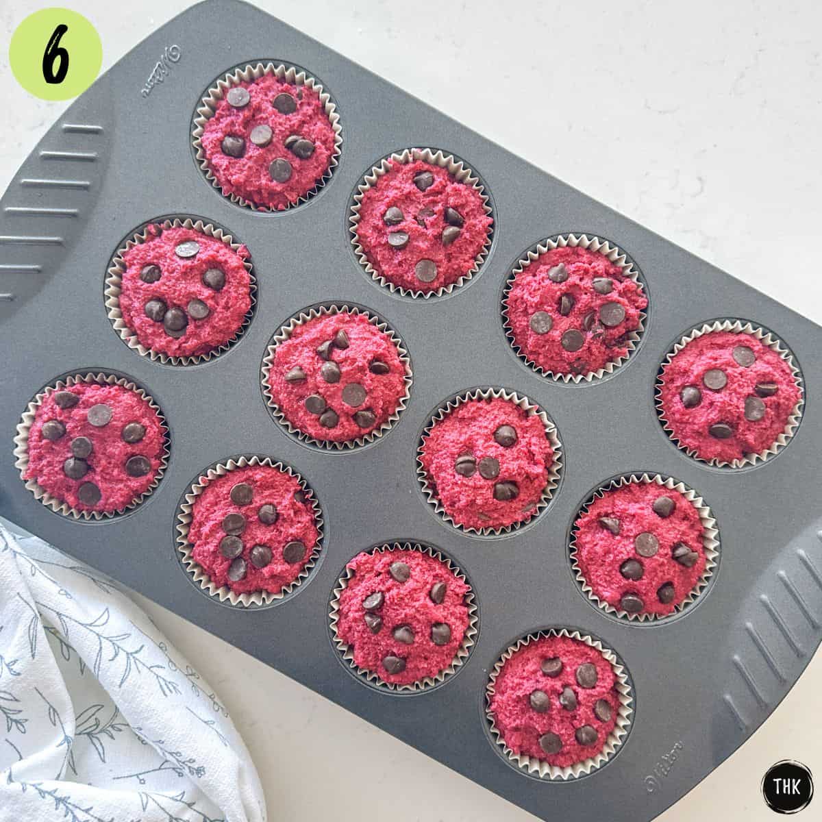 Unbaked pink muffins with chocolate chips inside muffin pan.