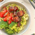 Bowl of zucchini noodles with broccoli, grape tomatoes and spicy tofu on top.