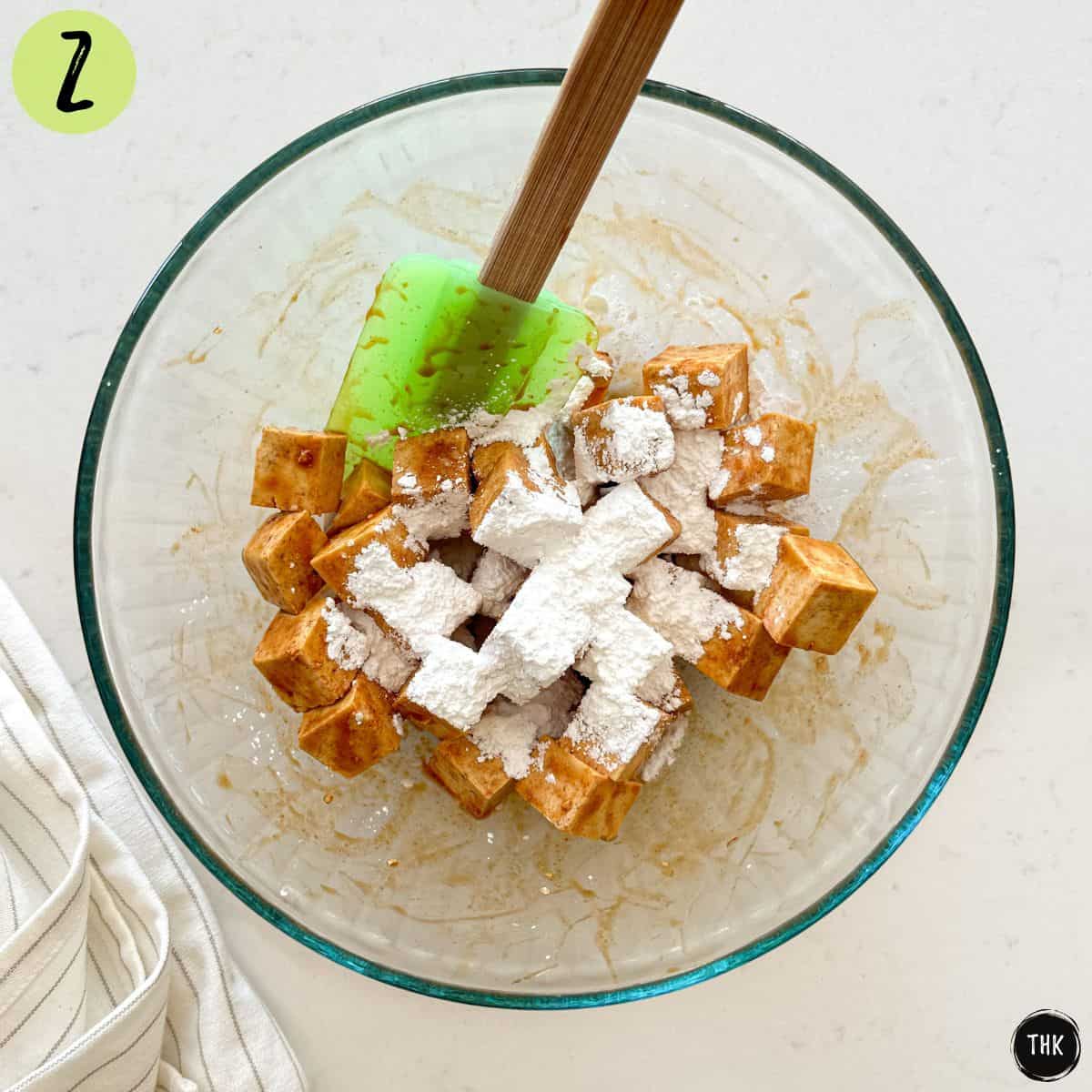 Cubed tofu in large glass bowl with spices and cornstarch.