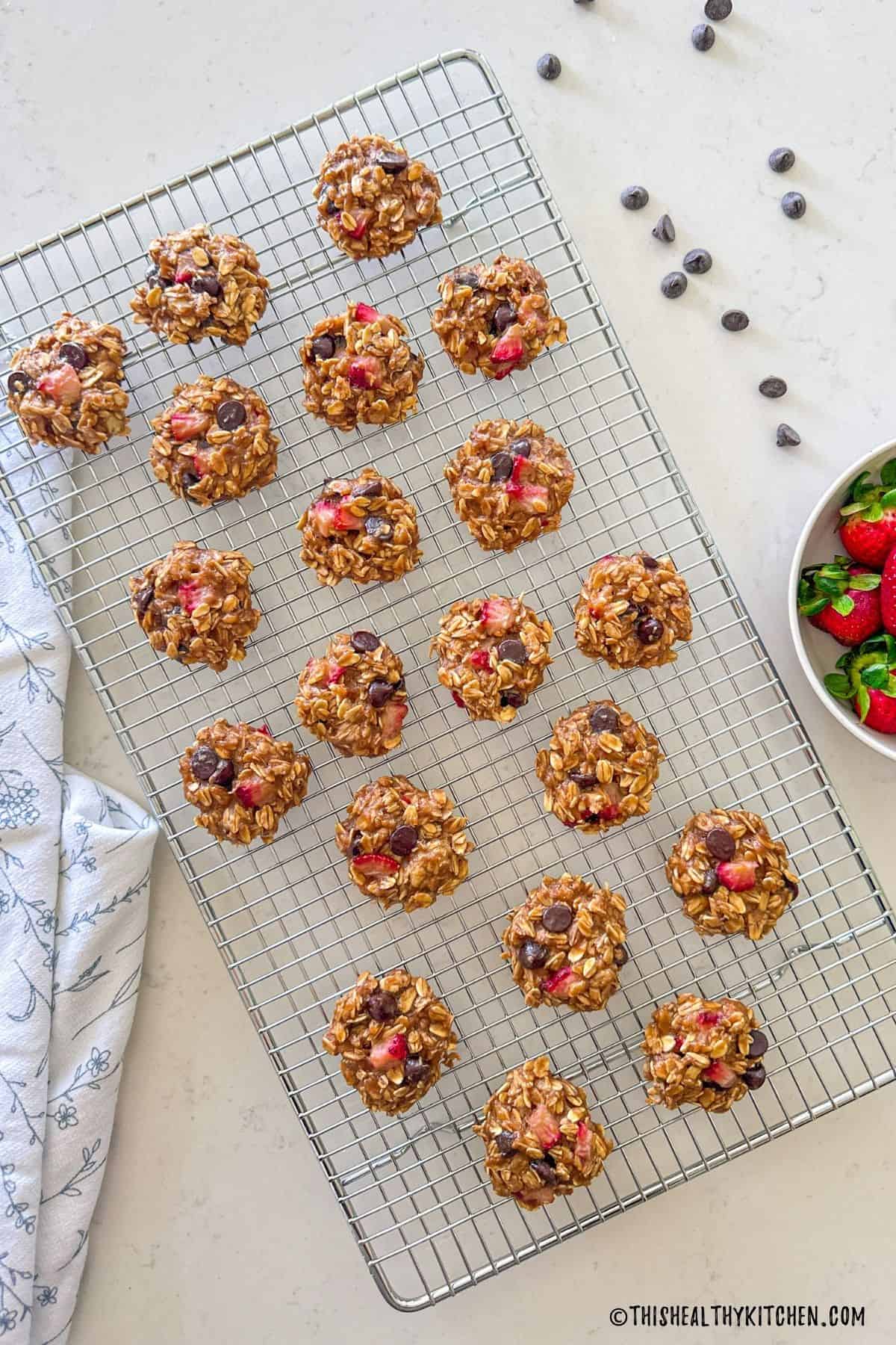 Vegan strawberry cookies with chocolate chips on cooling rack with bowl of strawberries beside it.