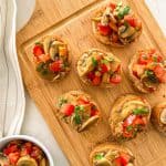 Mushroom bruschetta with fresh basil on top sitting on wooden cutting board.