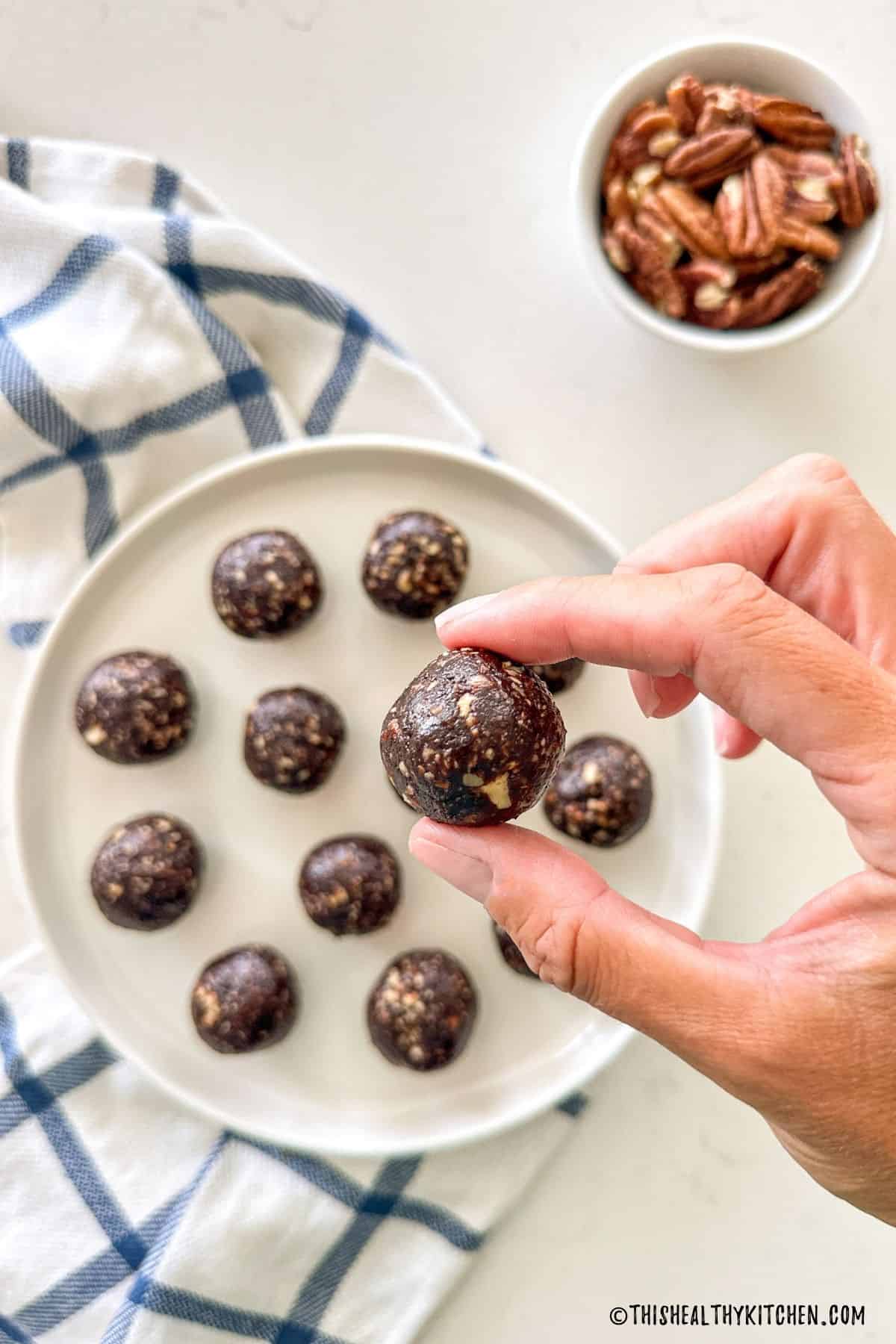 Chocolate mocha energy ball in hand with more balls in plate below.