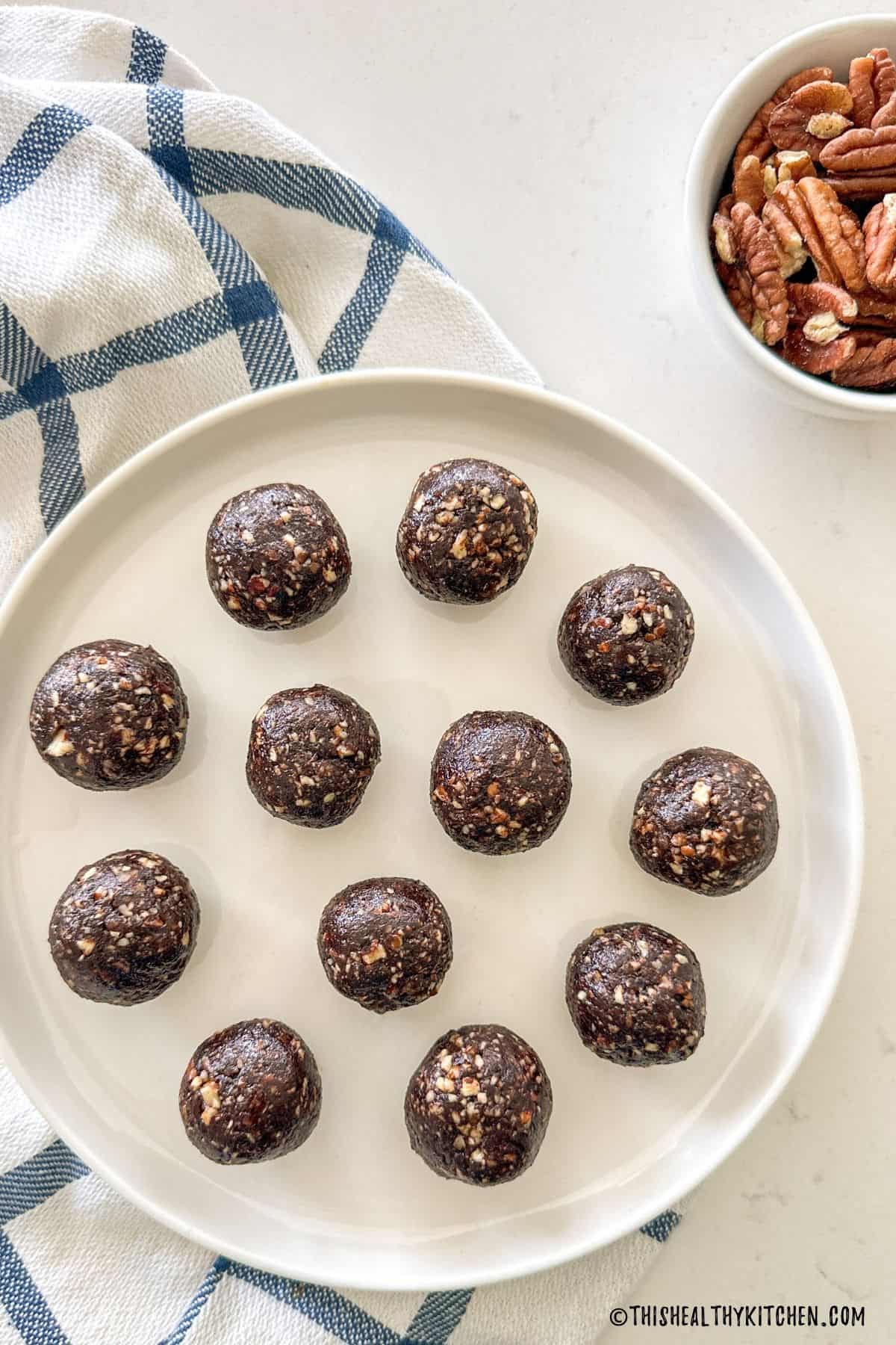 White plate with mocha bliss balls inside and bowl of pecans beside it.