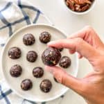 Chocolate mocha energy ball in hand with more balls in plate below.