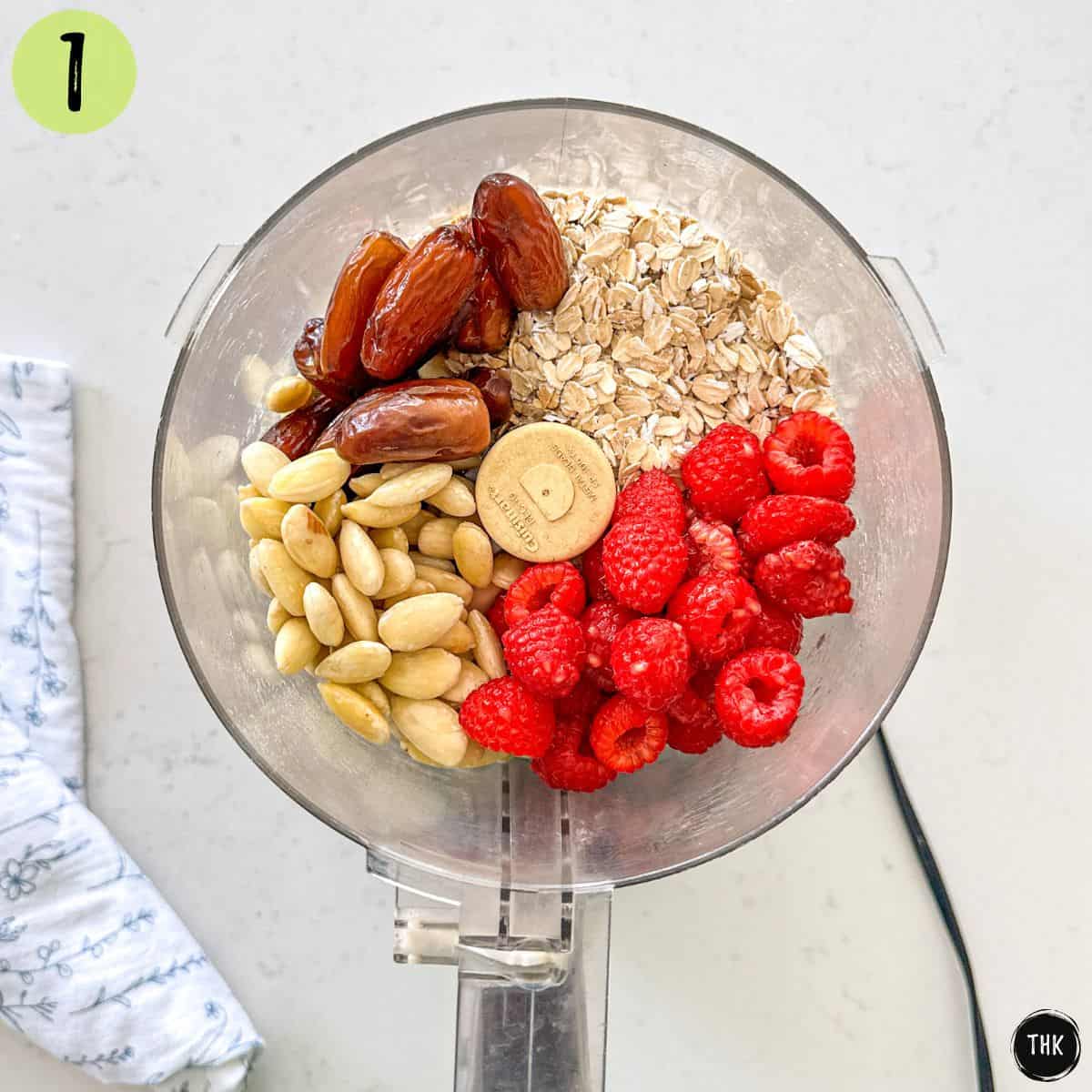 Food processor with raspberries, dates, oats, and blanched almonds inside.