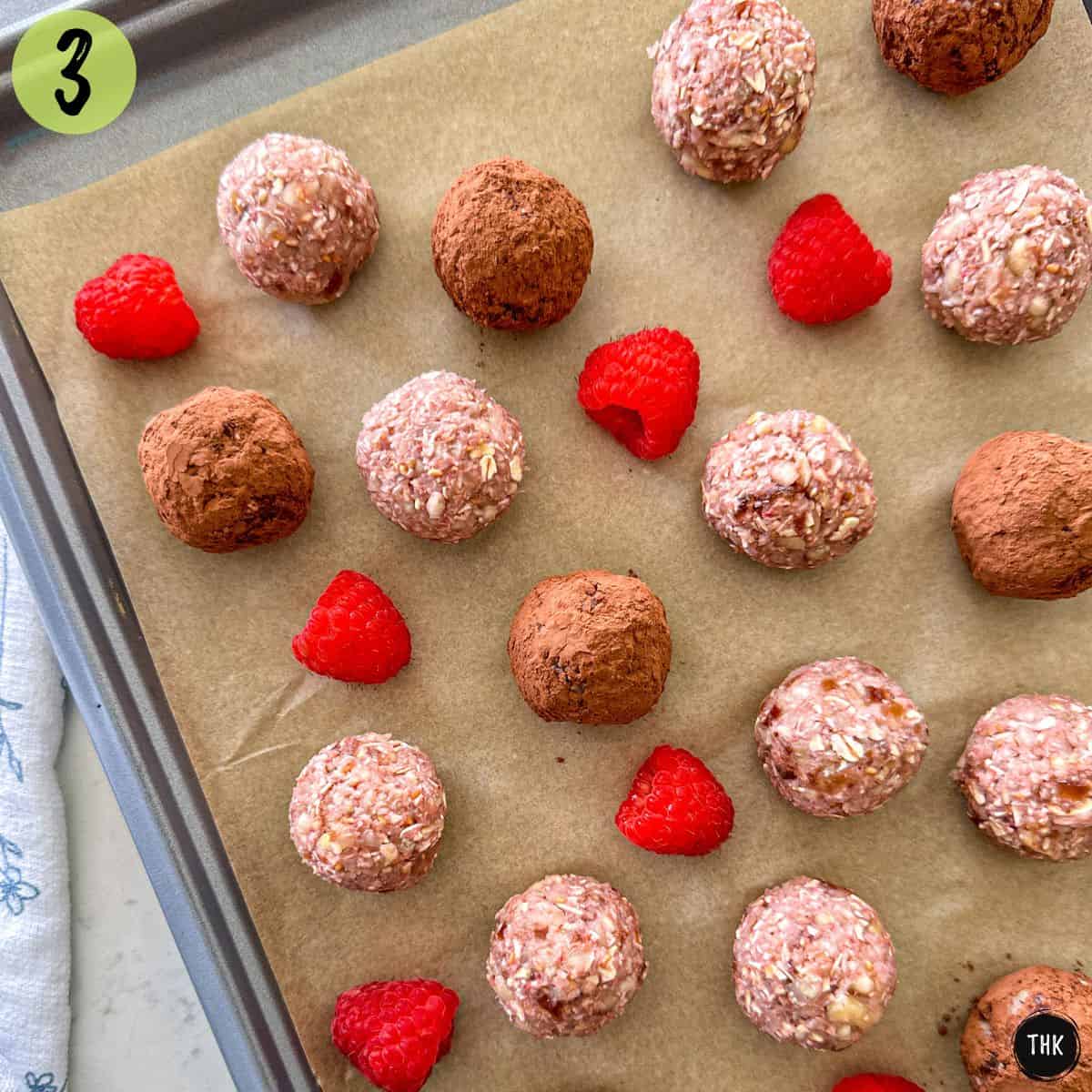 Baking sheet with raspberry bliss balls and fresh raspberries on top.