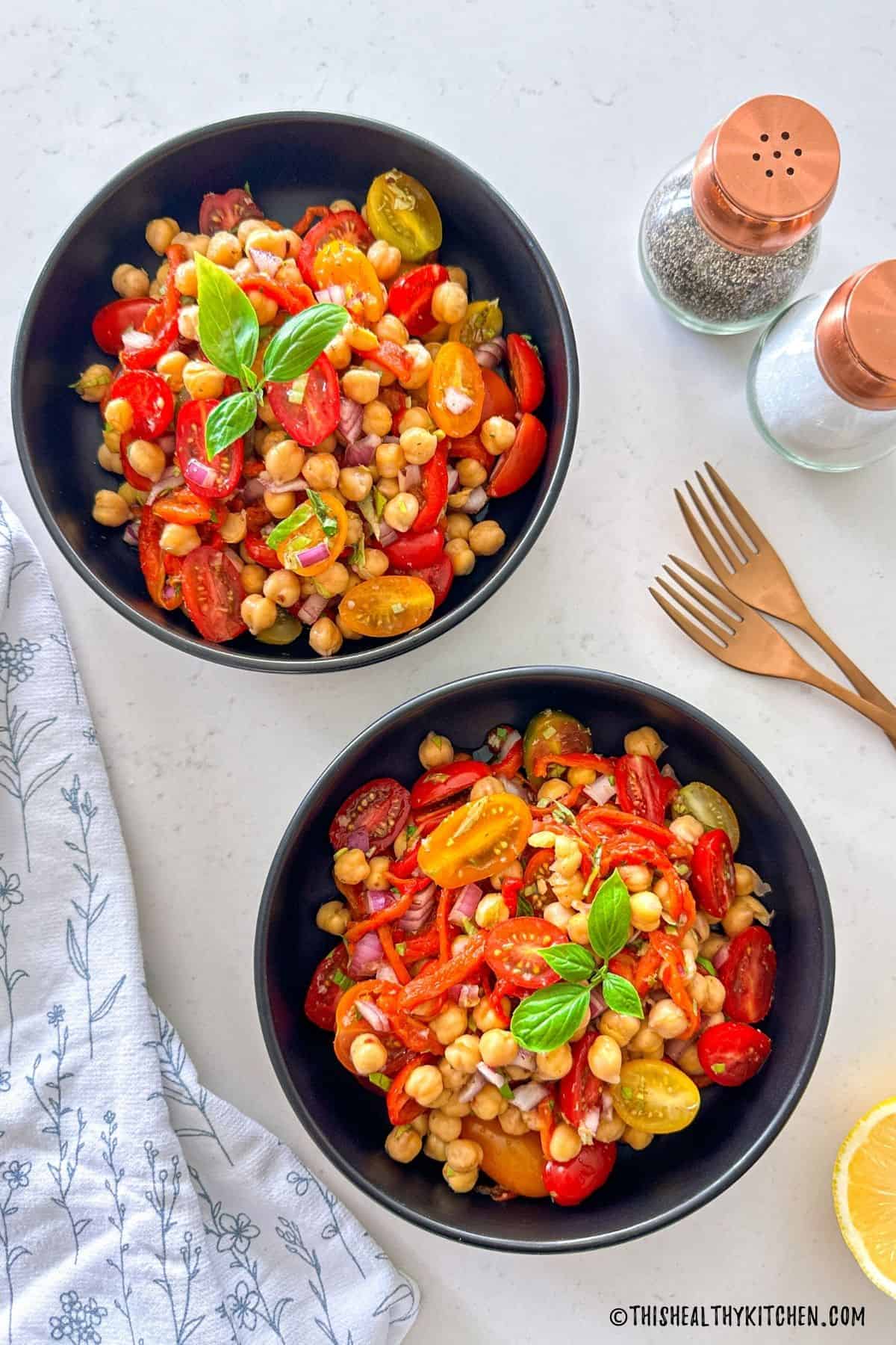 Two bowls of salad with roasted red peppers, chickpeas, cherry tomatoes, red onion, and basil.