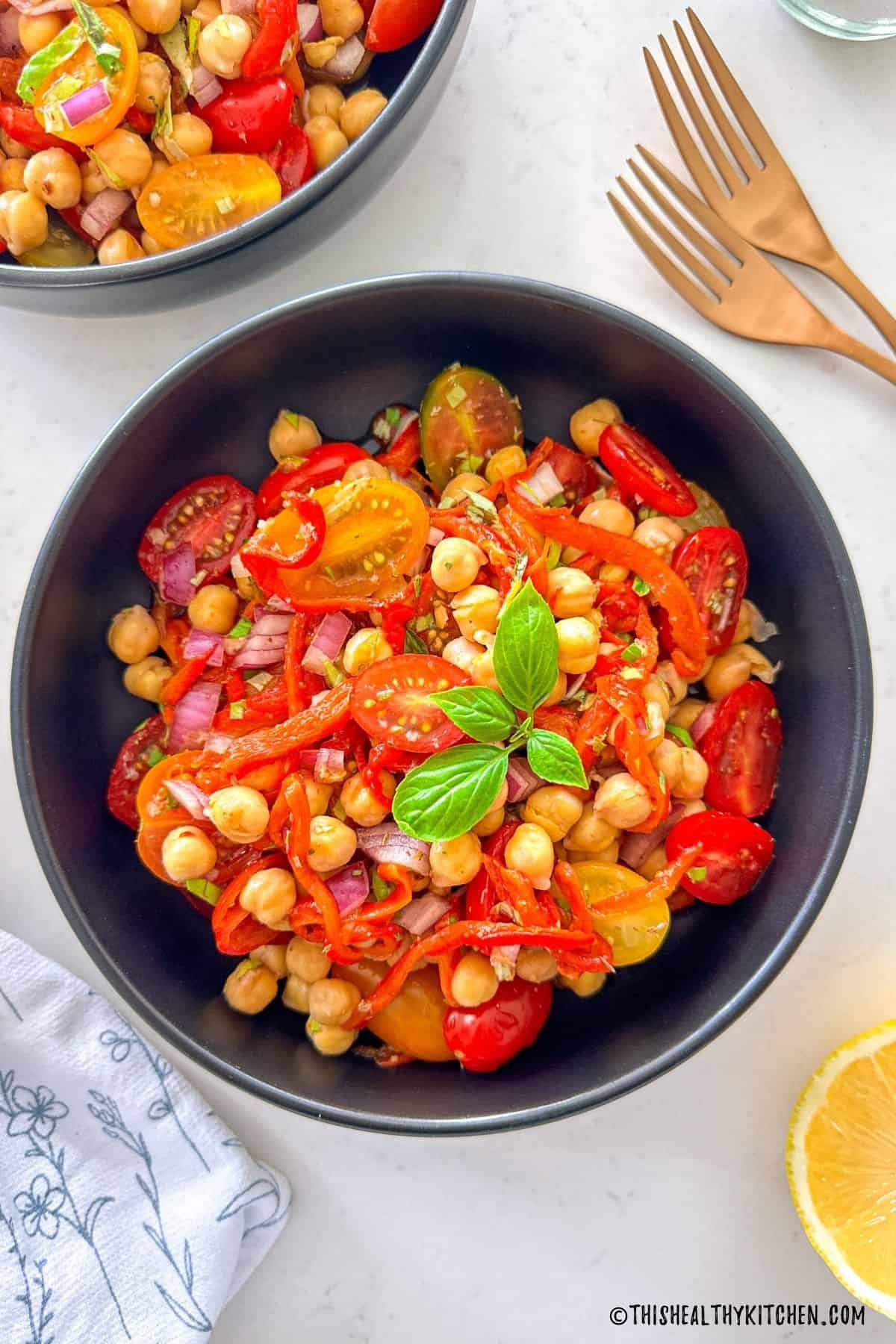Bowl of salad with roasted red peppers, chickpeas, cherry tomatoes, red onion, and basil.