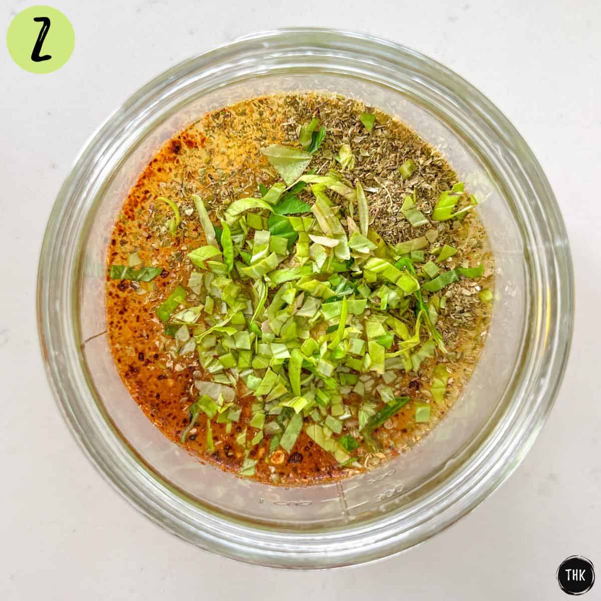 Glass jar with lemon juice, spices, and chopped basil.