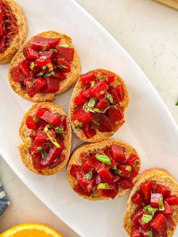 Beet bruschetta on white dish with fresh basil on top.