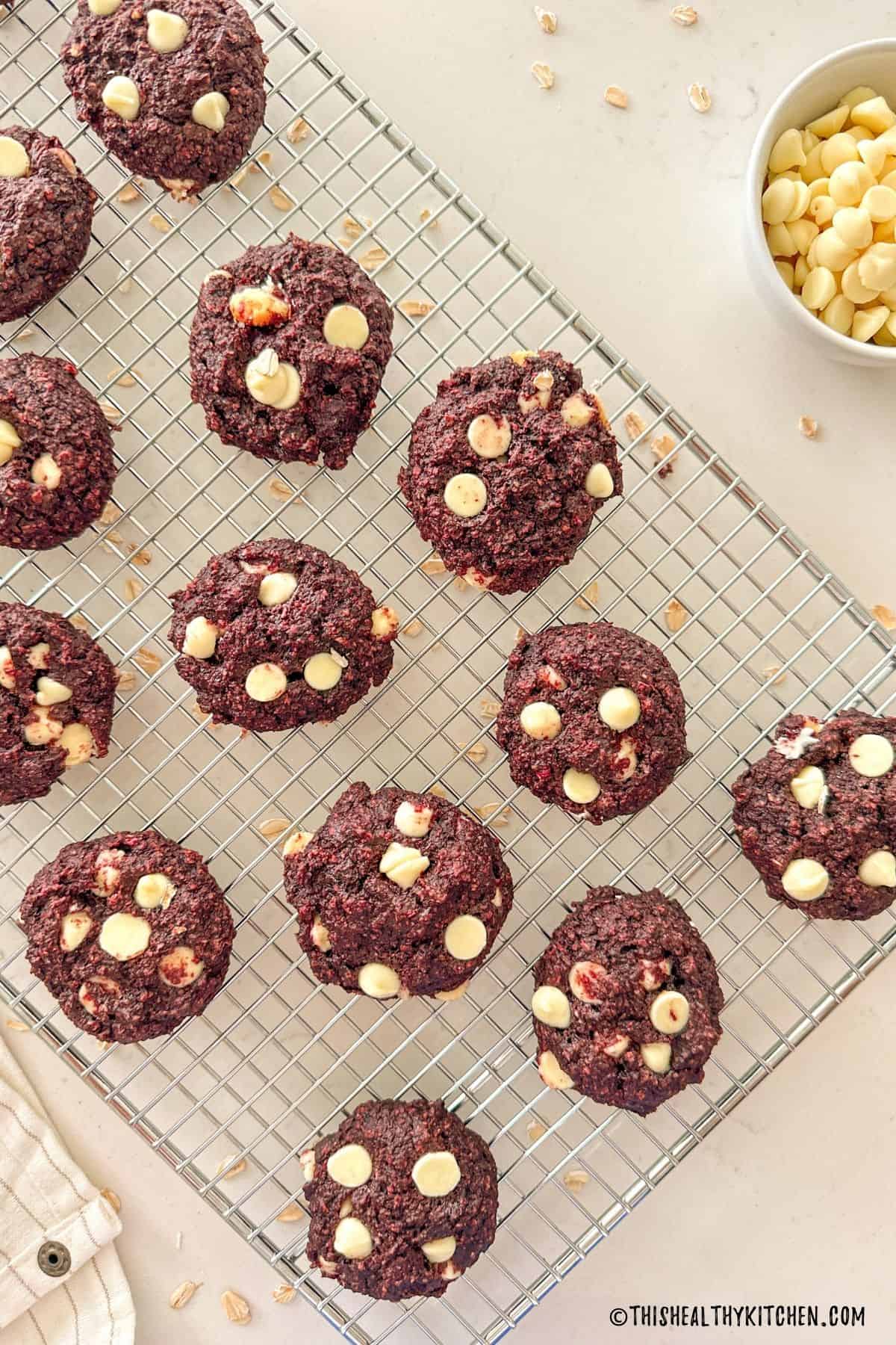 Vegan red velvet cookies with white chocolate chips on cooling rack.