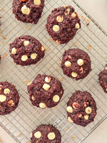 Vegan red velvet cookies with white chocolate chips on cooling rack.