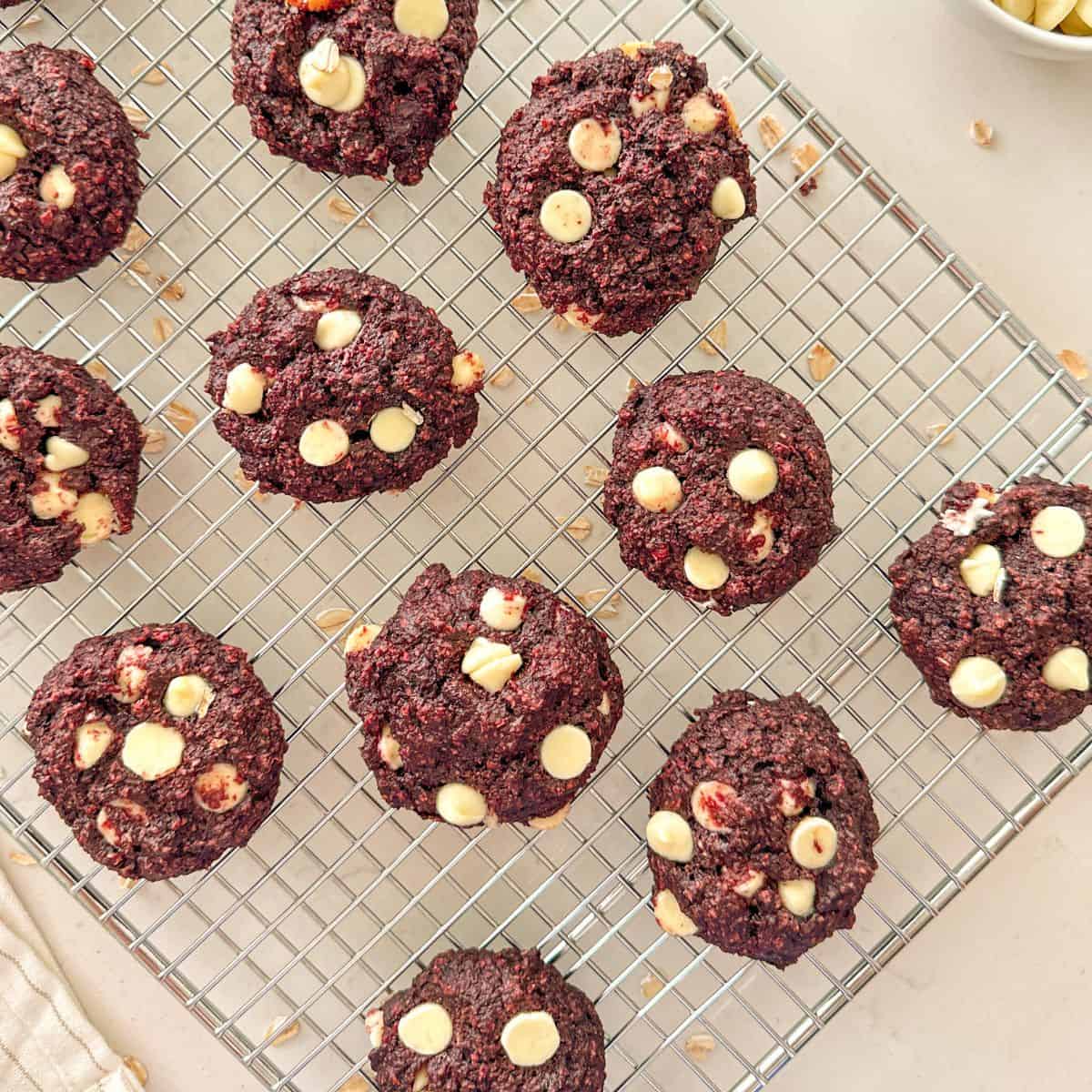 Vegan red velvet cookies with white chocolate chips on cooling rack.