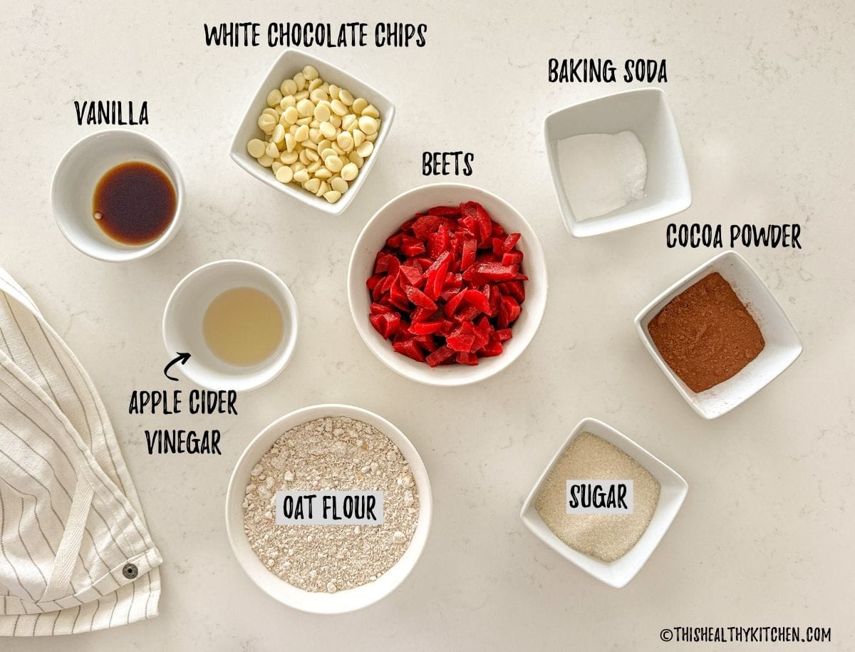 Prep bowls with beets, flour, sugar, vinegar, vanilla, cocoa powder, baking soda and white chocolate chips on countertop.