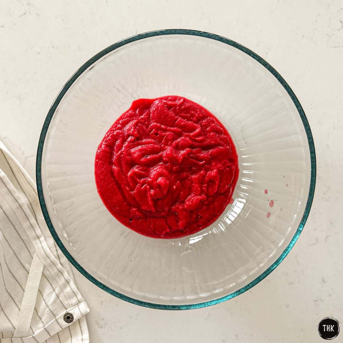 Glass mixing bowl with red batter inside.
