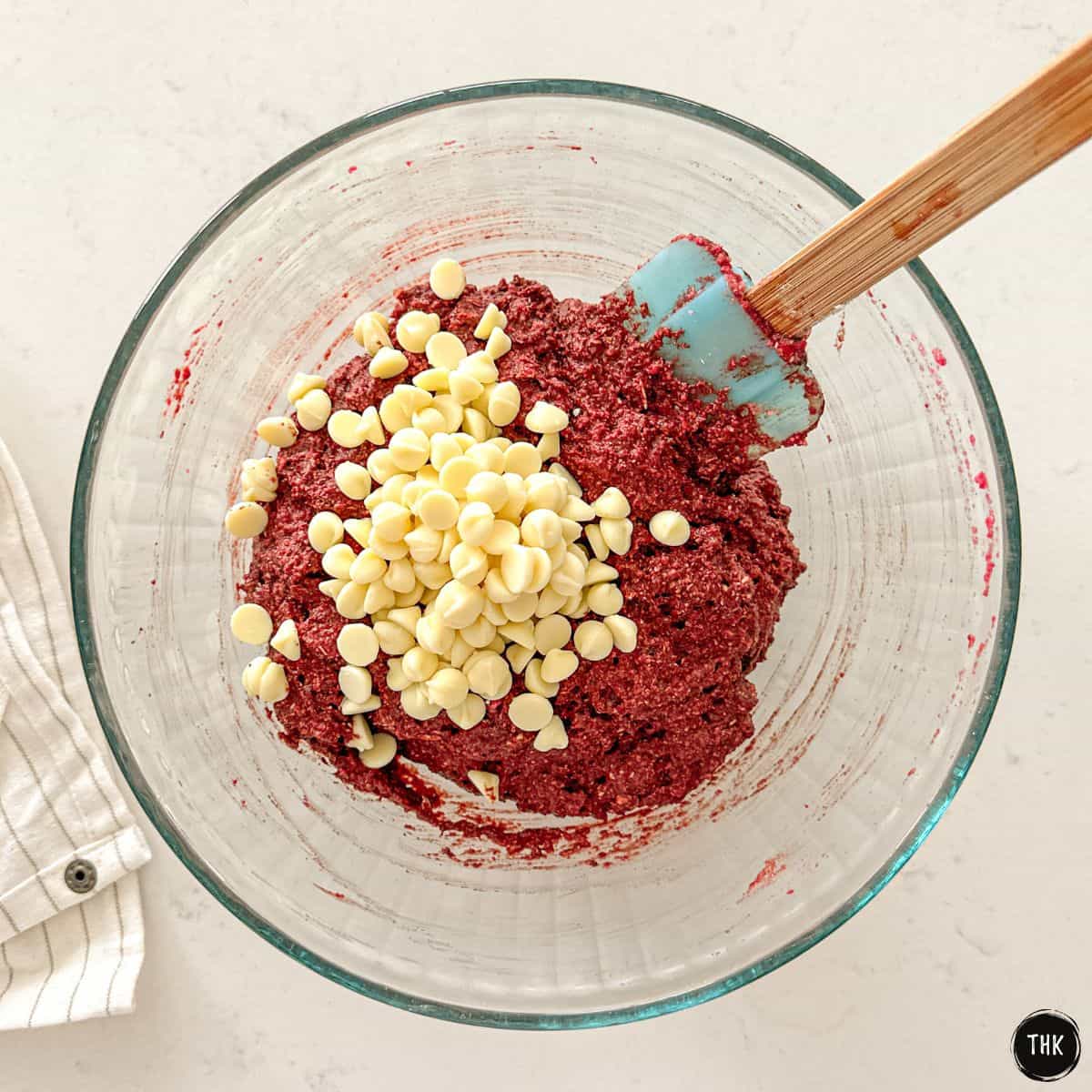 Red beet cookie batter in glass bowl with white chocolate chips on top.