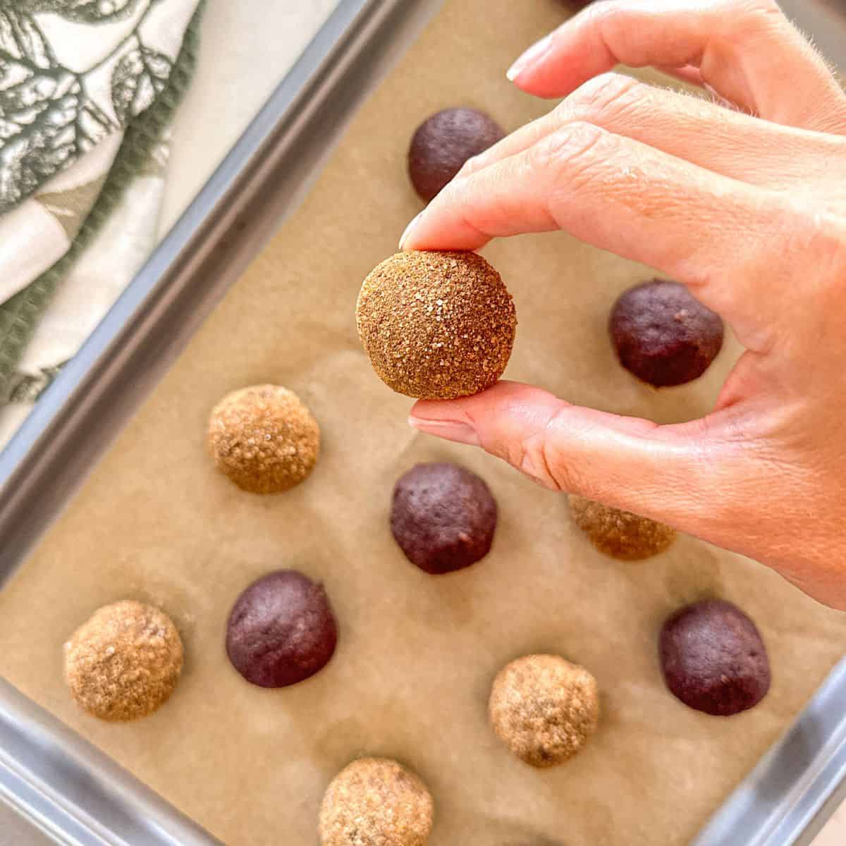 Hand picking up a pumpkin bliss ball from baking sheet.