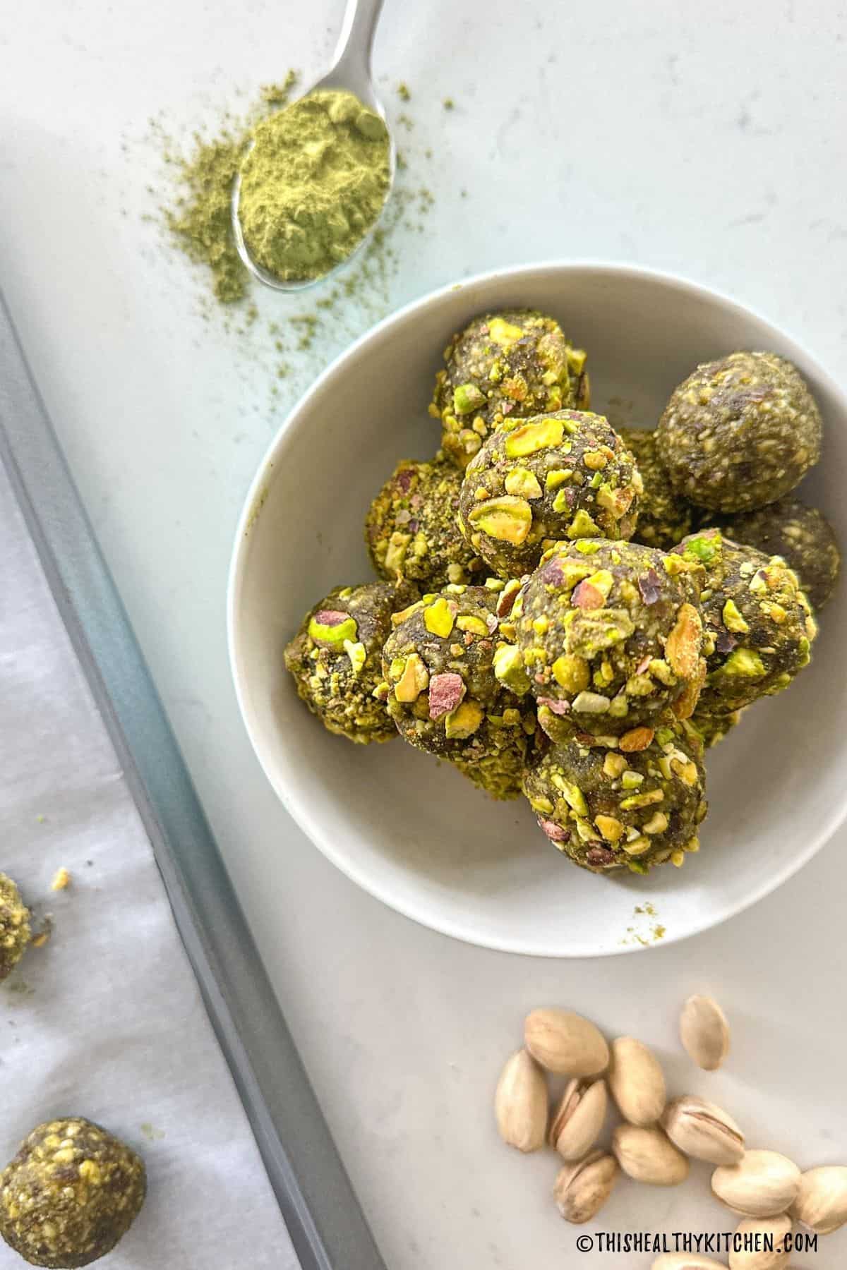 Bowl of matcha energy balls with spoon of matcha powder beside it.