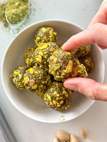 Hand reaching for matcha energy ball from bowl.