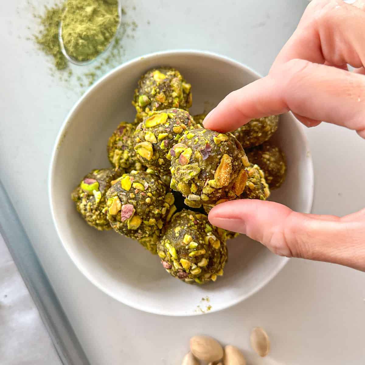 Hand reaching for matcha energy ball from bowl.