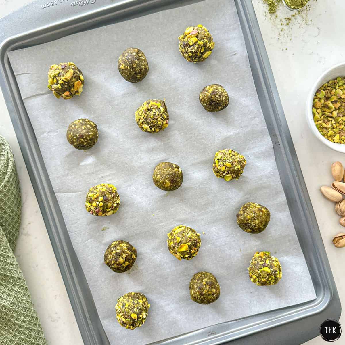 Matcha energy balls on baking sheet, half of which are rolled into crushed pistachios.