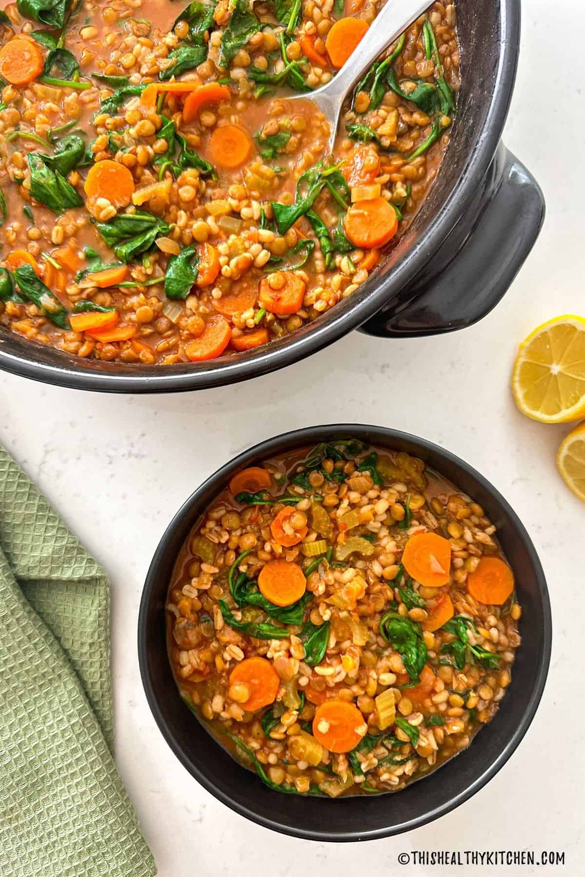 Pot of barley and lentil soup with vegetables and bowl of soup beside it.