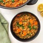 Pot of barley and lentil soup with vegetables and bowl of soup beside it.