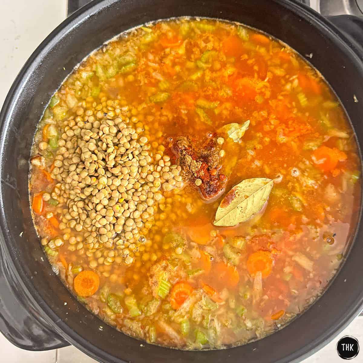 Large ceramic skillet with sautéed veggies, lentils, barley and broth inside.