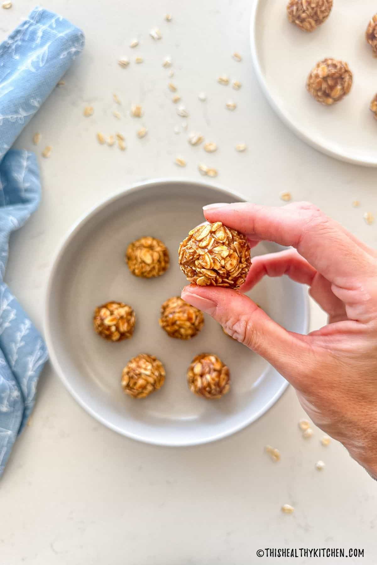Hand holding up an oatmeal energy ball with more of them in a bowl below.