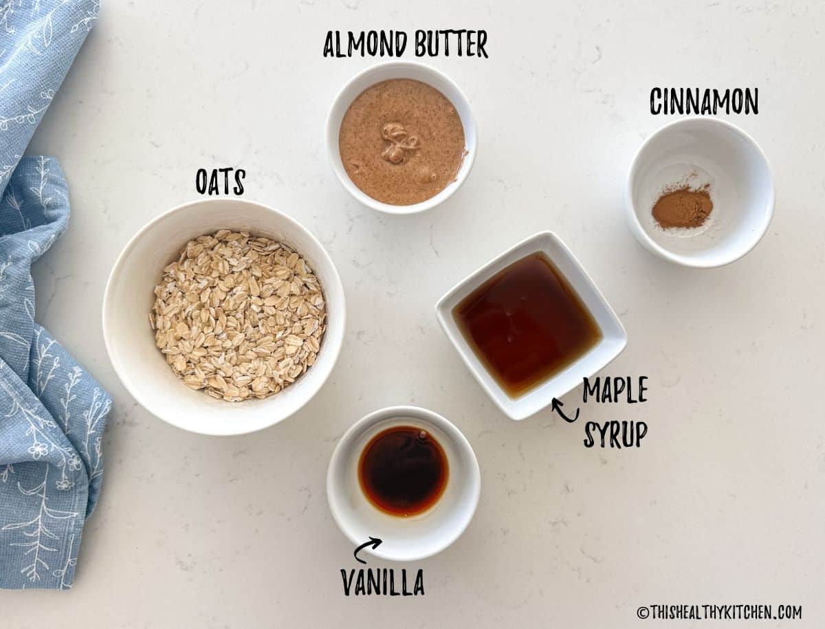 Oats, almond butter, vanilla, maple syrup, and cinnamon in prep bowls on countertop.